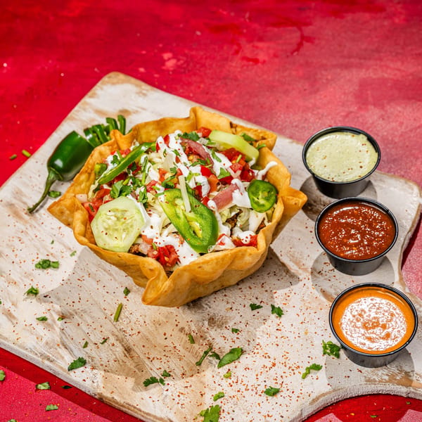A Chubby's Tacos taco salad in a crispy shell with three dipping sauces on a wooden board.