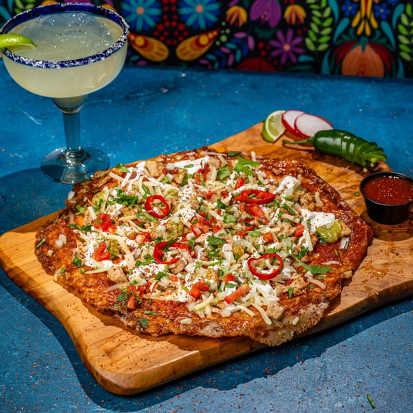 Chubby's Tacos' loaded chicken enchilada on a wooden board with a margarita and salsa.