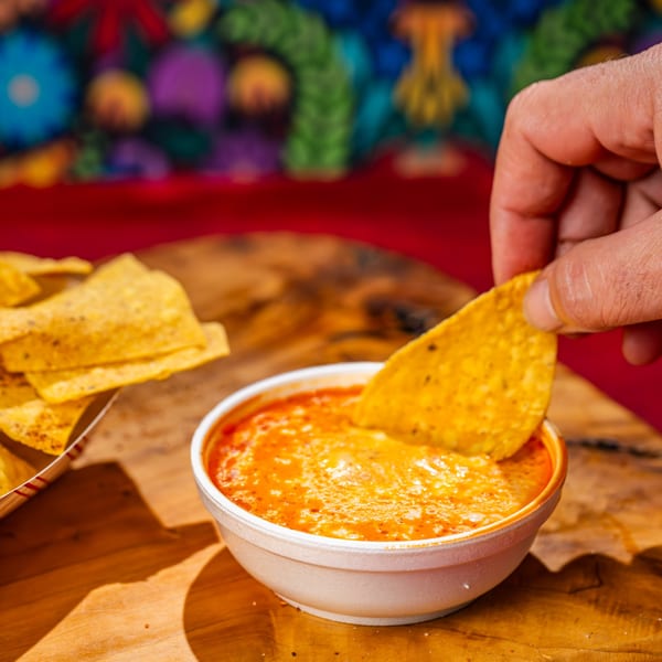A hand dips a tortilla chip into a bowl of Chubby's Tacos queso dip.