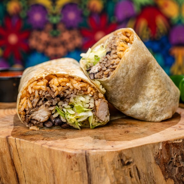 Two Chubby's Tacos burritos, filled with rice, beans, chicken, and lettuce, on a wooden surface.