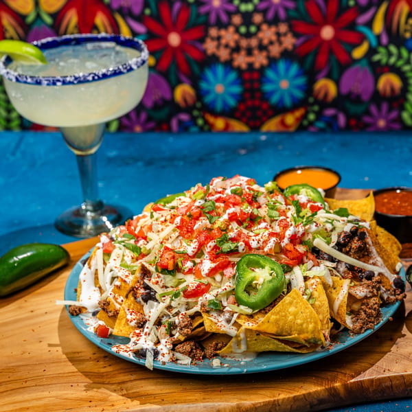 A large plate of Chubby's Tacos nachos with a margarita against a colorful floral background.