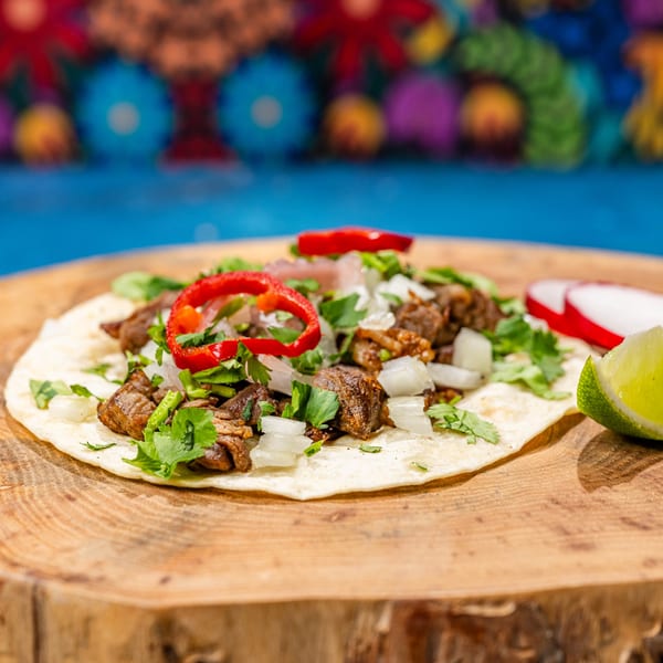 A Chubby's Tacos carne asada taco with onions, cilantro, and red peppers on a wooden board.