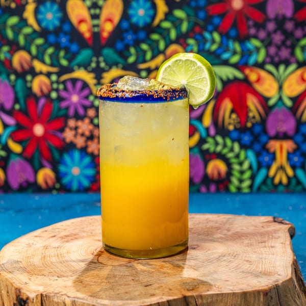 A Chubby's Tacos mango margarita with a chili-lime rim and lime wedge on a wooden slab.